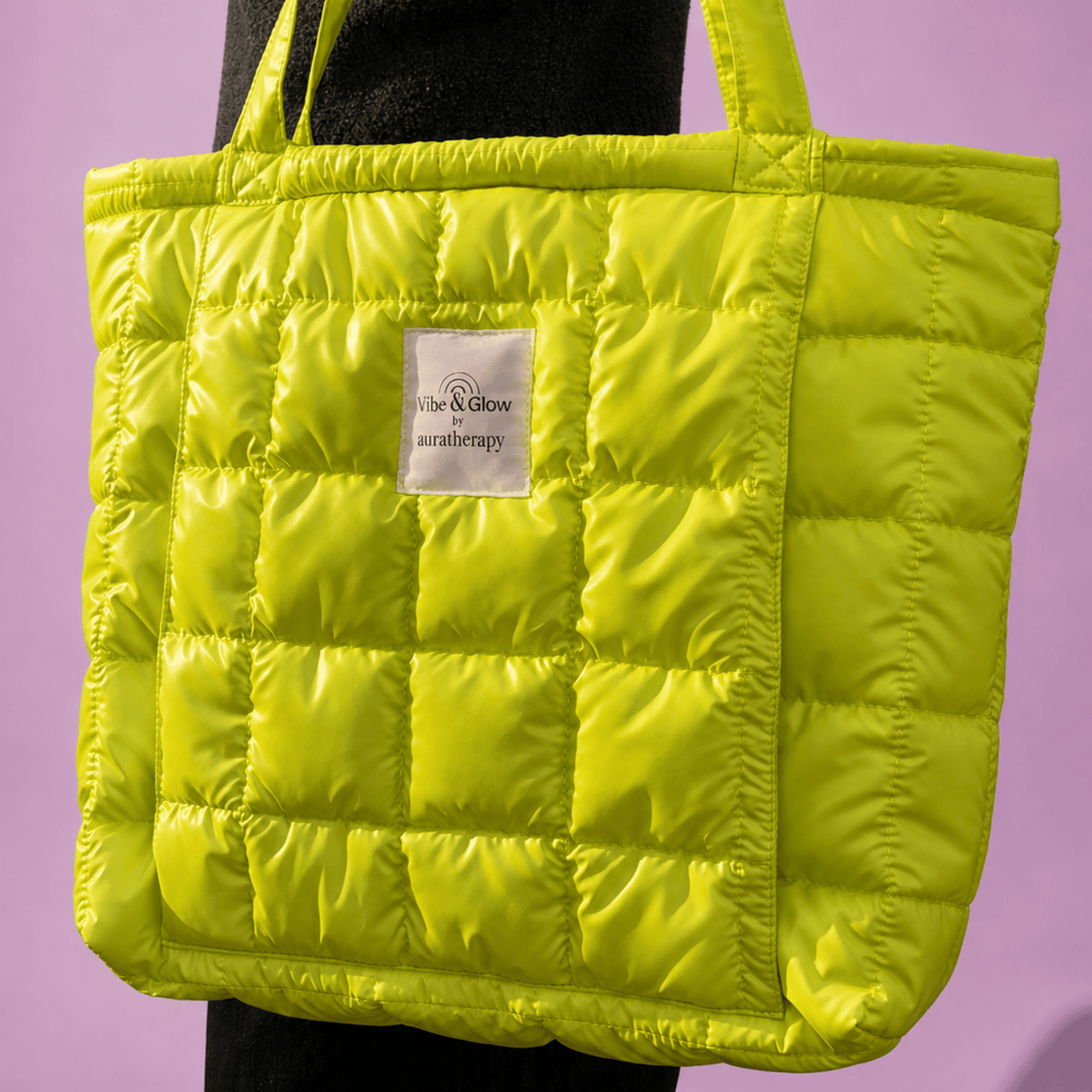 A bright lime green quilted puffer tote bag with a white brand label reading 'Vibe & Glow & saratherapy', shown against a solid lavender background.