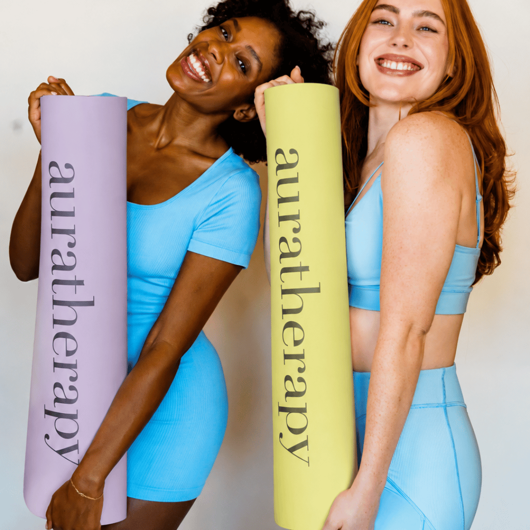 Two women holding yoga mats with 'auratherapy' branding against a plain background